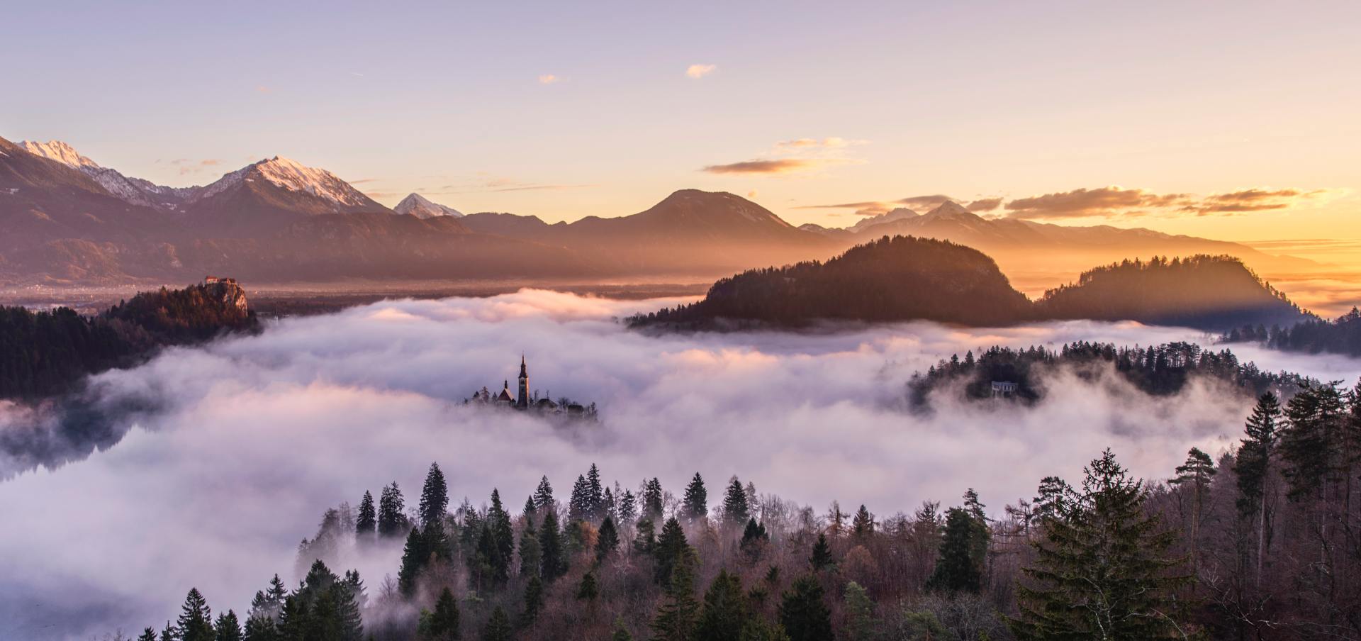 A sunset over a lake filled with fog and mountains in the background
