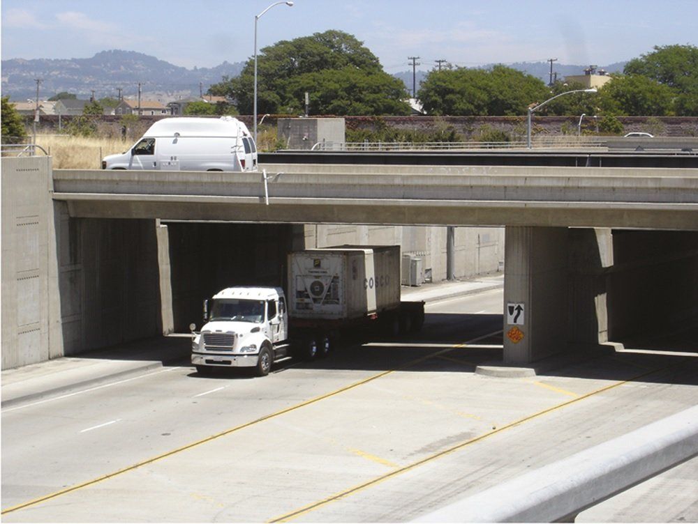 A white truck is driving under a bridge with the number 44 on the side