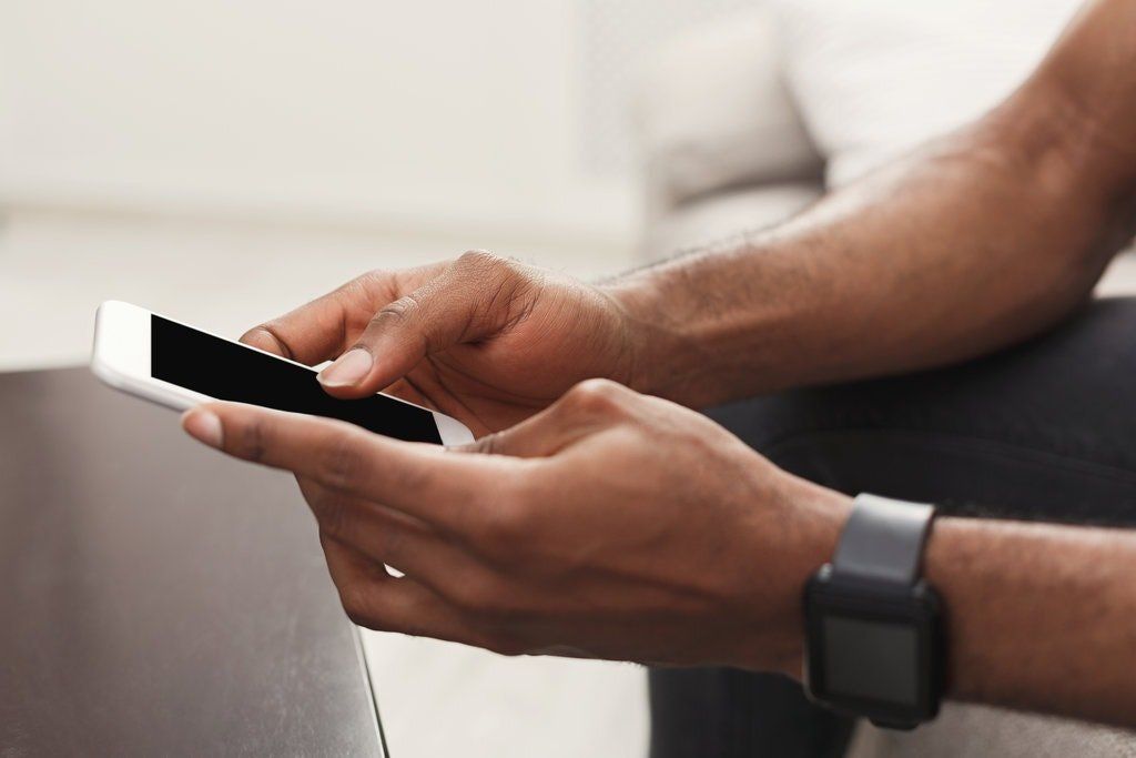 A man is sitting on a couch using a smart phone.