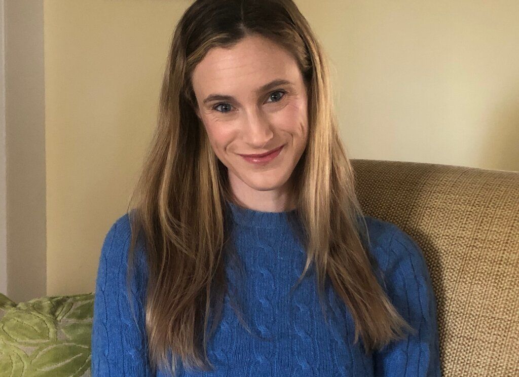A woman in a blue sweater is sitting in a chair and smiling.