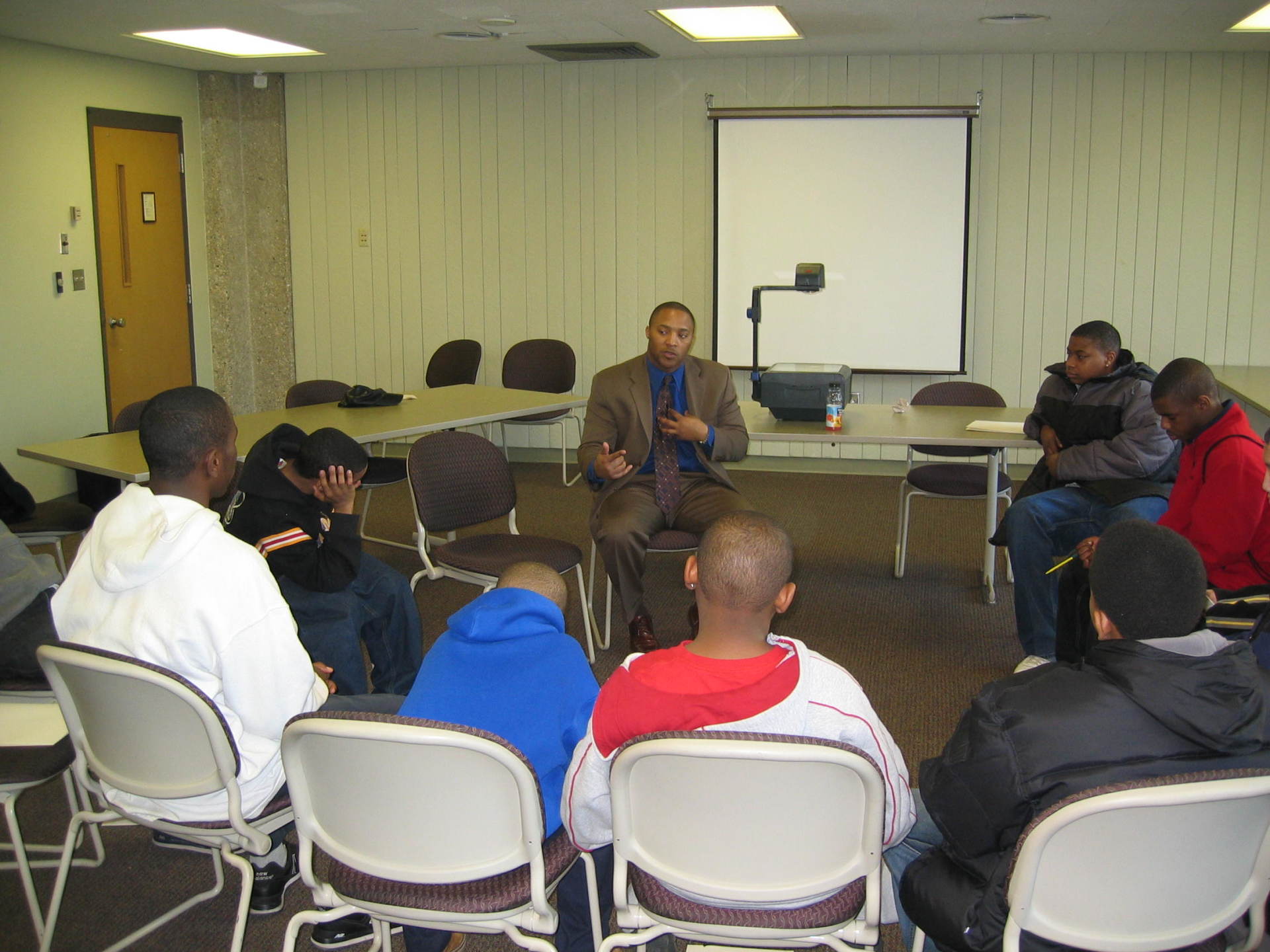 Speaker sitting and speaking to room filled with students at previous Positive Images Leadership Teen Summit meeting in Milwaukee