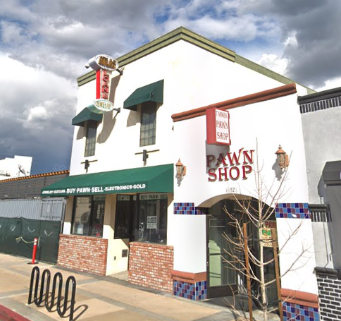 Pawn shop building with green awnings, a red sign, and a bike rack on a sunny day.