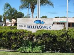 City of Bellflower sign with blue logo, set against greenery and a sunny sky.