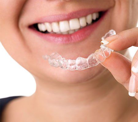 Invisalign — Smiling Female Holding Transparent Teeth Braces in Tenafly, NJ Invisalign — Smiling Female Holding Transparent Teeth Braces in Tenafly, NJ