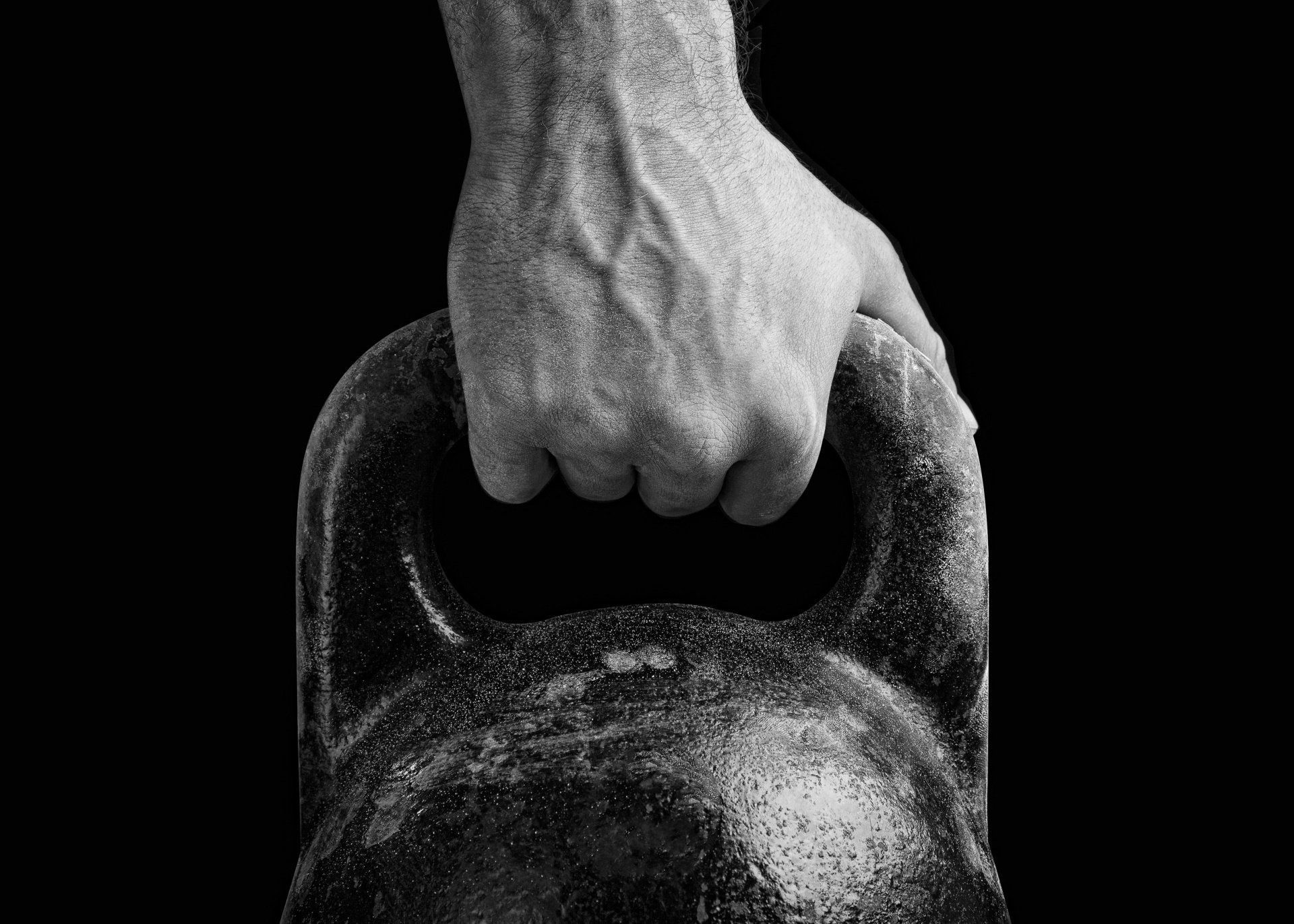 A black and white photo of a man 's hand holding a kettlebell.