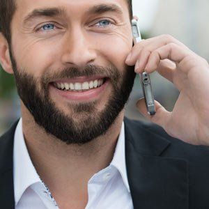 Contact Solution Web Designs, A Leading Responsive, Mobile-Friendly Website Development - Man in a suit smiles while talking on a phone. He has a full beard and blue eyes.
