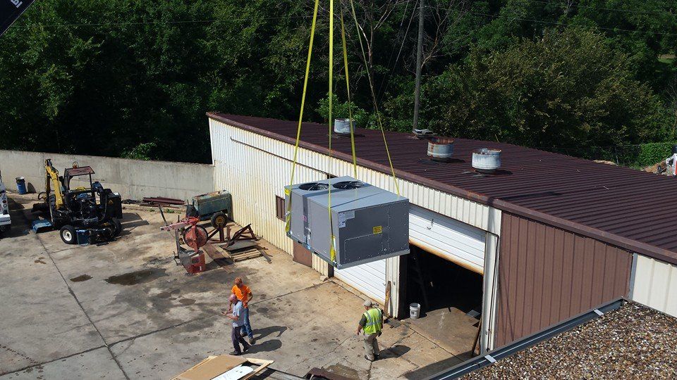 Crane lifting HVAC unit onto the roof of a building with workers present.