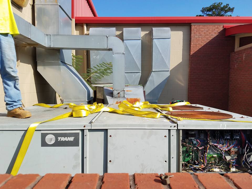 HVAC unit on a rooftop with ductwork and yellow straps; person standing nearby.