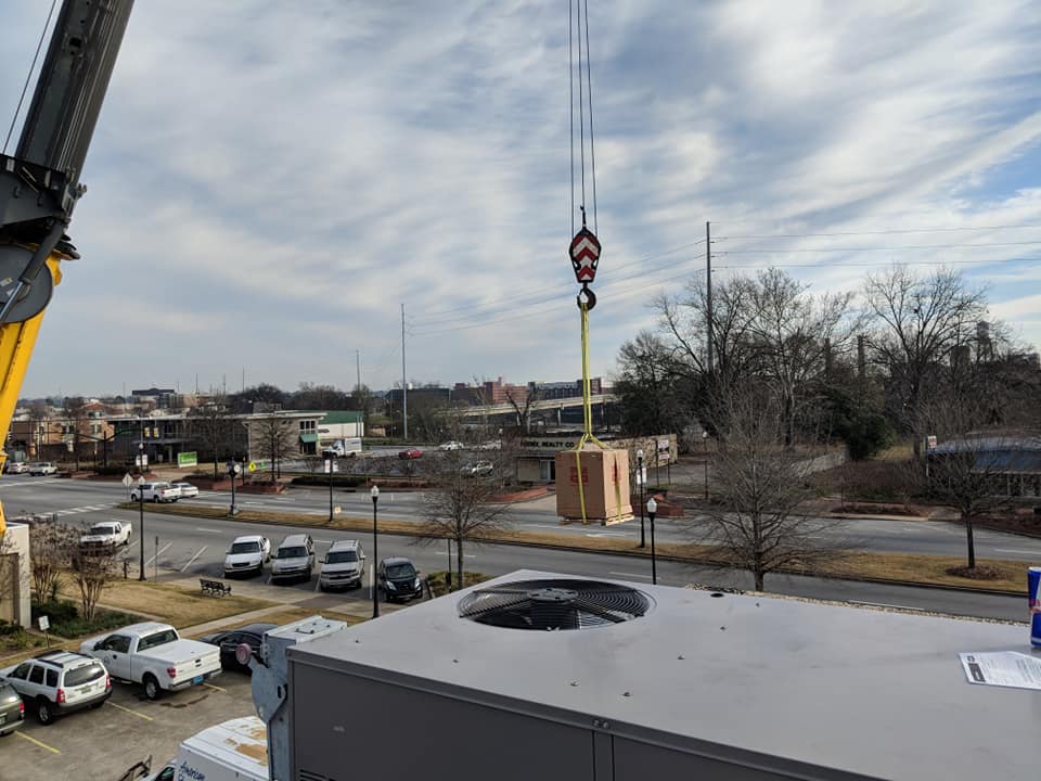 Crane lifting a large, wooden structure over a city street on a cloudy day.