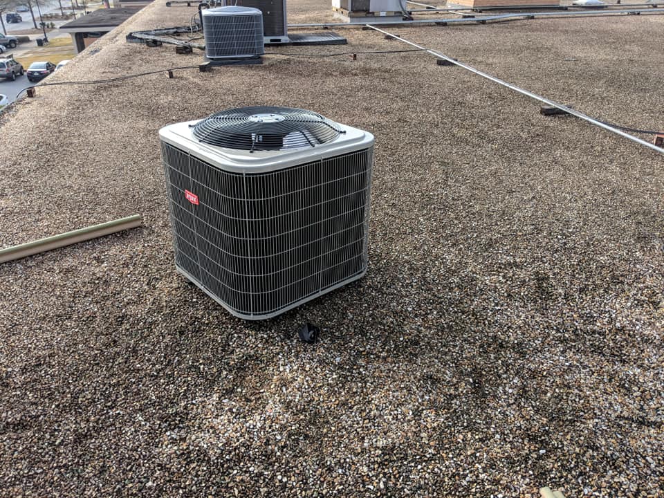An air conditioning unit sits on a gravel-covered flat roof.
