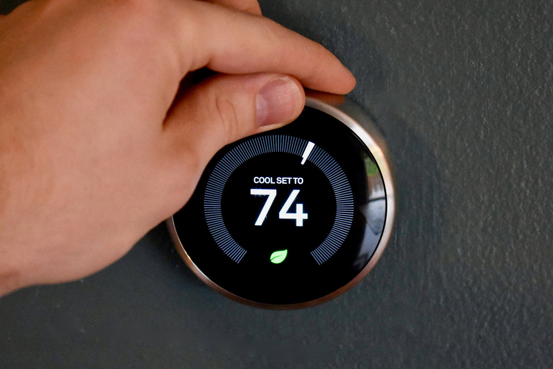 Hand turning a smart thermostat dial, setting to 74 degrees, with a leaf icon lit.