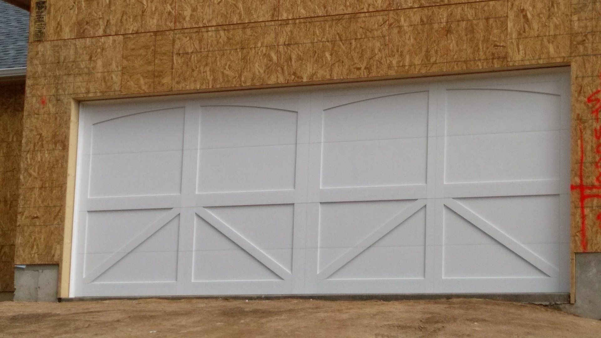 A white garage door is sitting on the side of a house under construction.