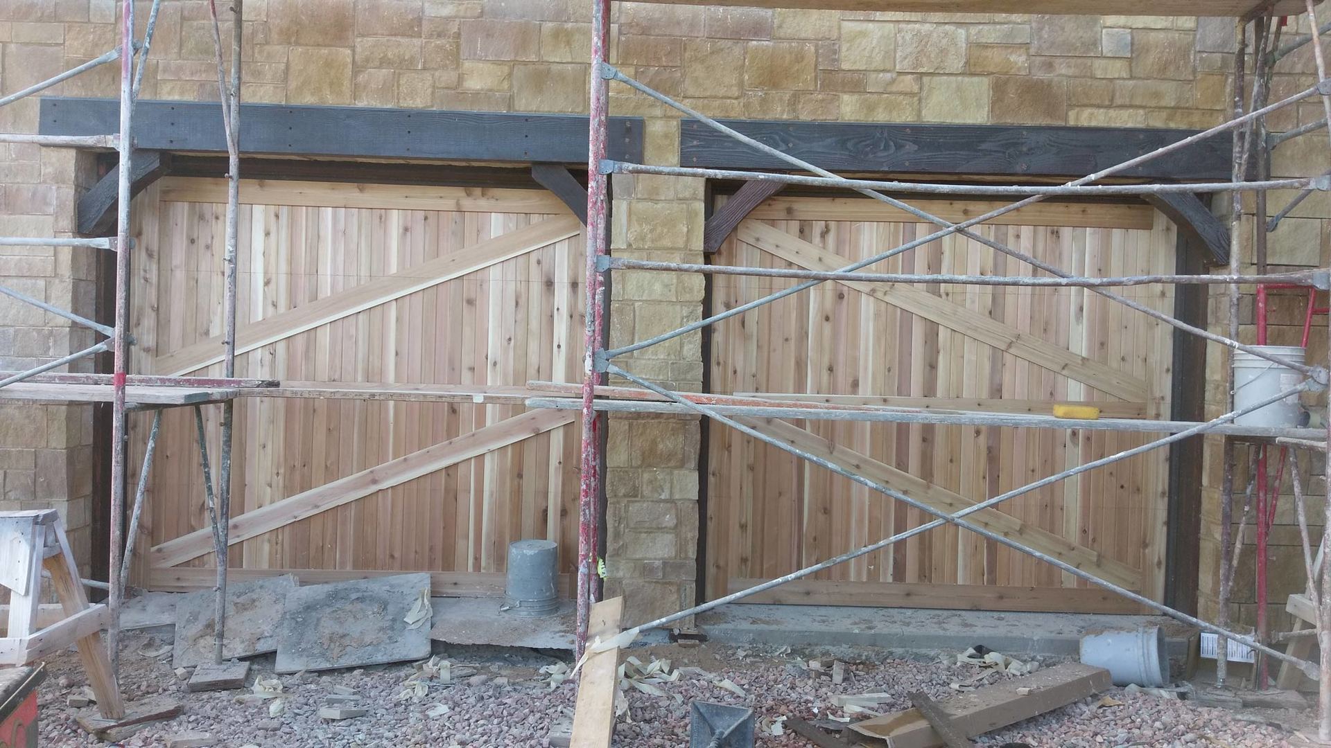 Two wooden garage doors that are under construction, surrounded by scaffolding.