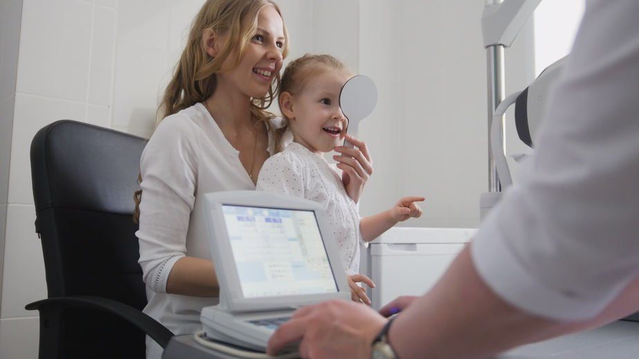 Woman holding young child on her lap while an optometrist performs a pediatric eye exam