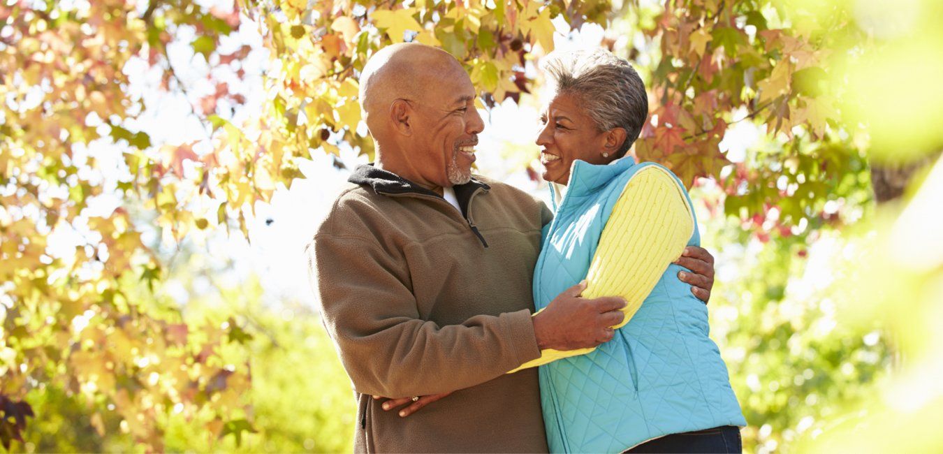 An elderly couple is hugging each other in a park.