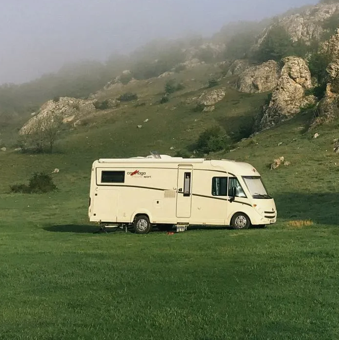 A white motorhome is parked on green grass with a hilly, foggy landscape in the background.