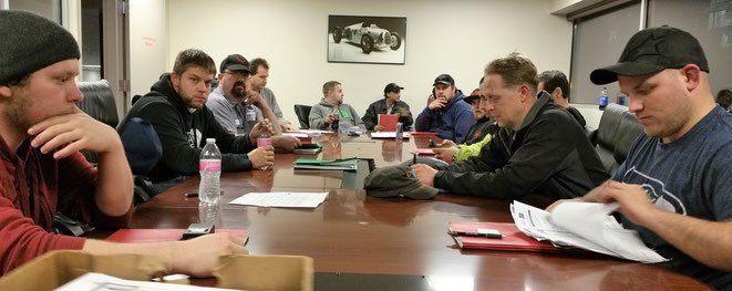 A group of people sitting around a conference table, some looking at papers, others looking at each other.