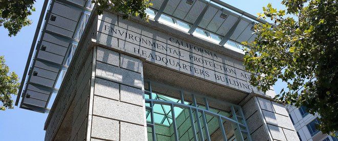 Stone building facade with etched text, glass windows, and a metal overhang under a blue sky.