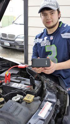 Man holding a jump starter, connected to a car battery. The setting is outdoors.