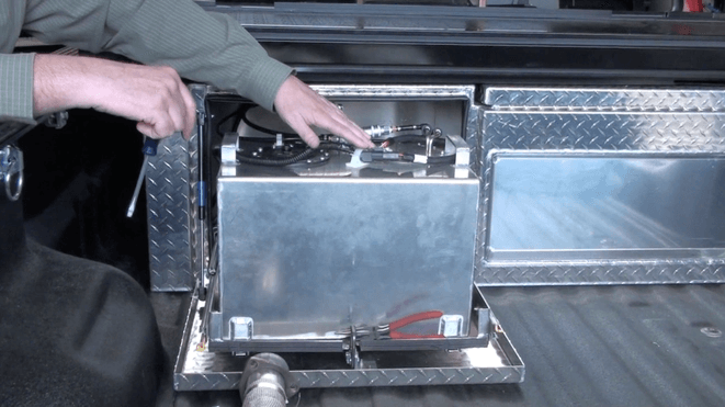 Person working on a metal tank in a truck bed. The tank is in a diamond-plated box.