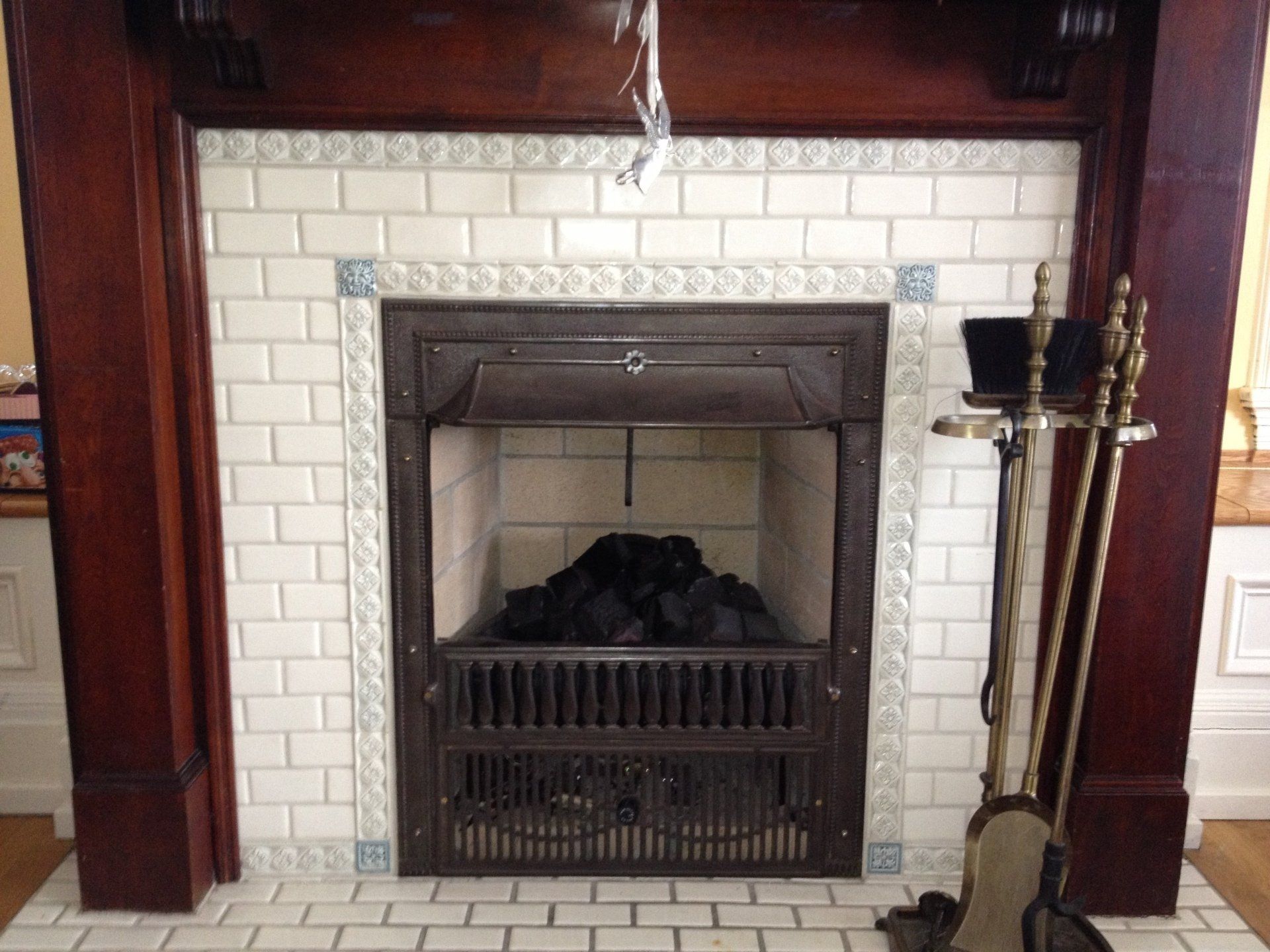 Fireplace with white tiled surround, dark wood mantel, and black interior. Fireplace tools on the right.