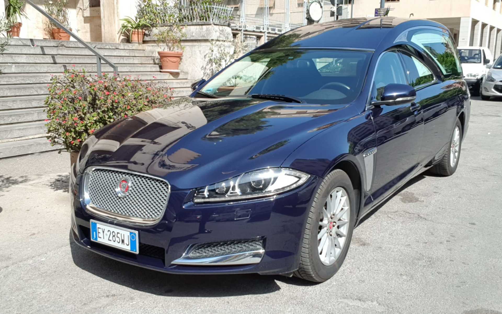 Carro funebre Blue Jaguar parcheggiato davanti a un edificio con gradini.
