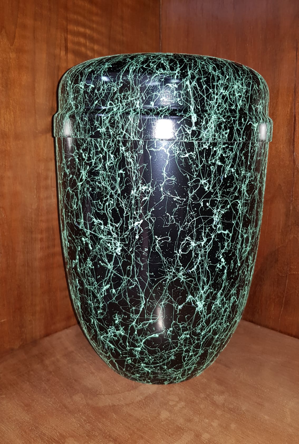 Urna maculata di nero e verde, con parte superiore e inferiore arrotondate, appoggiata su una superficie di legno.