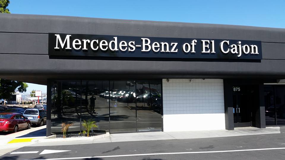 Mercedes-Benz of El Cajon dealership storefront with large sign and black facade. Glass windows reveal cars inside.