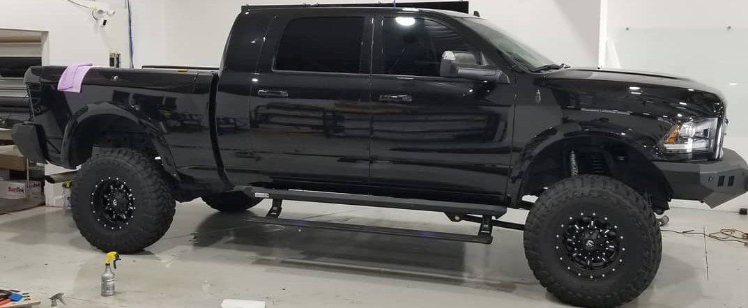 Black lifted pickup truck, black wheels, side steps. In a garage setting.