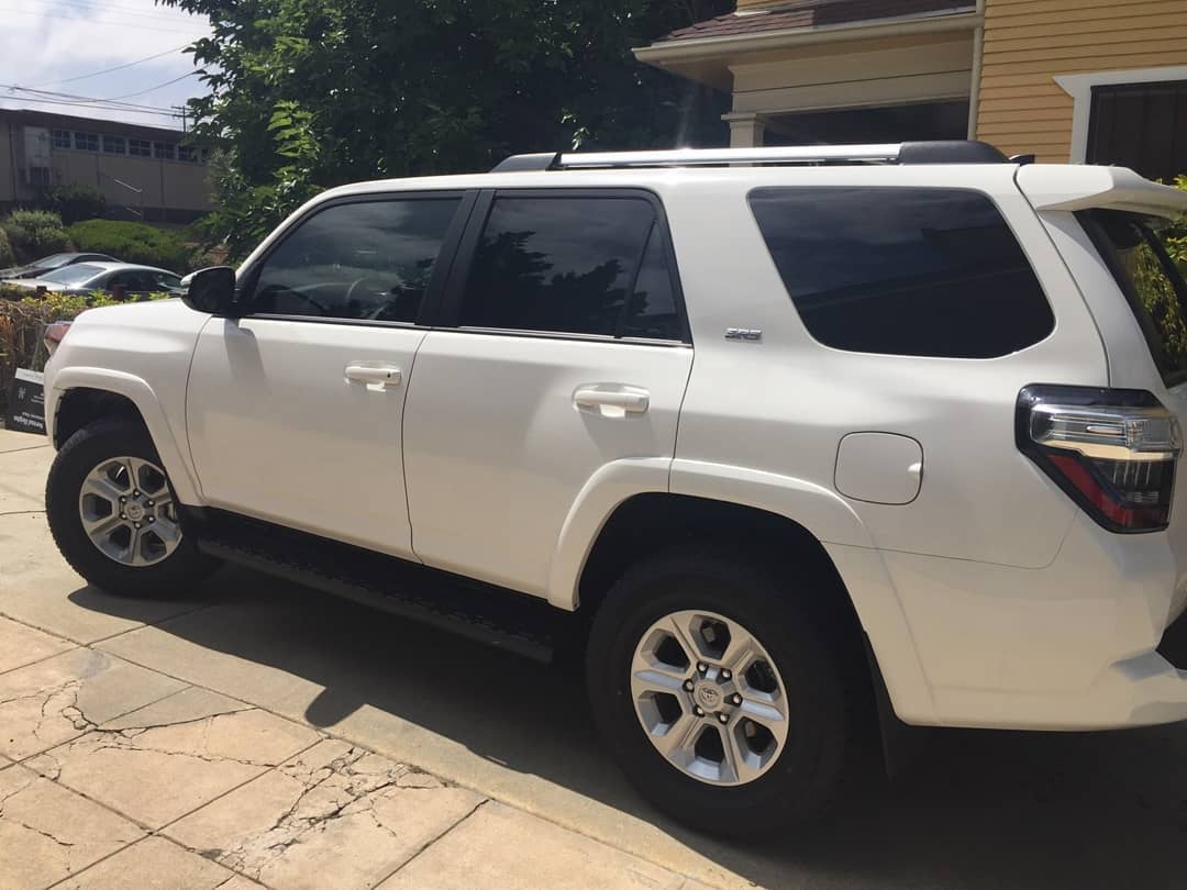 White Toyota 4Runner SUV parked on a paved driveway in front of a yellow house.