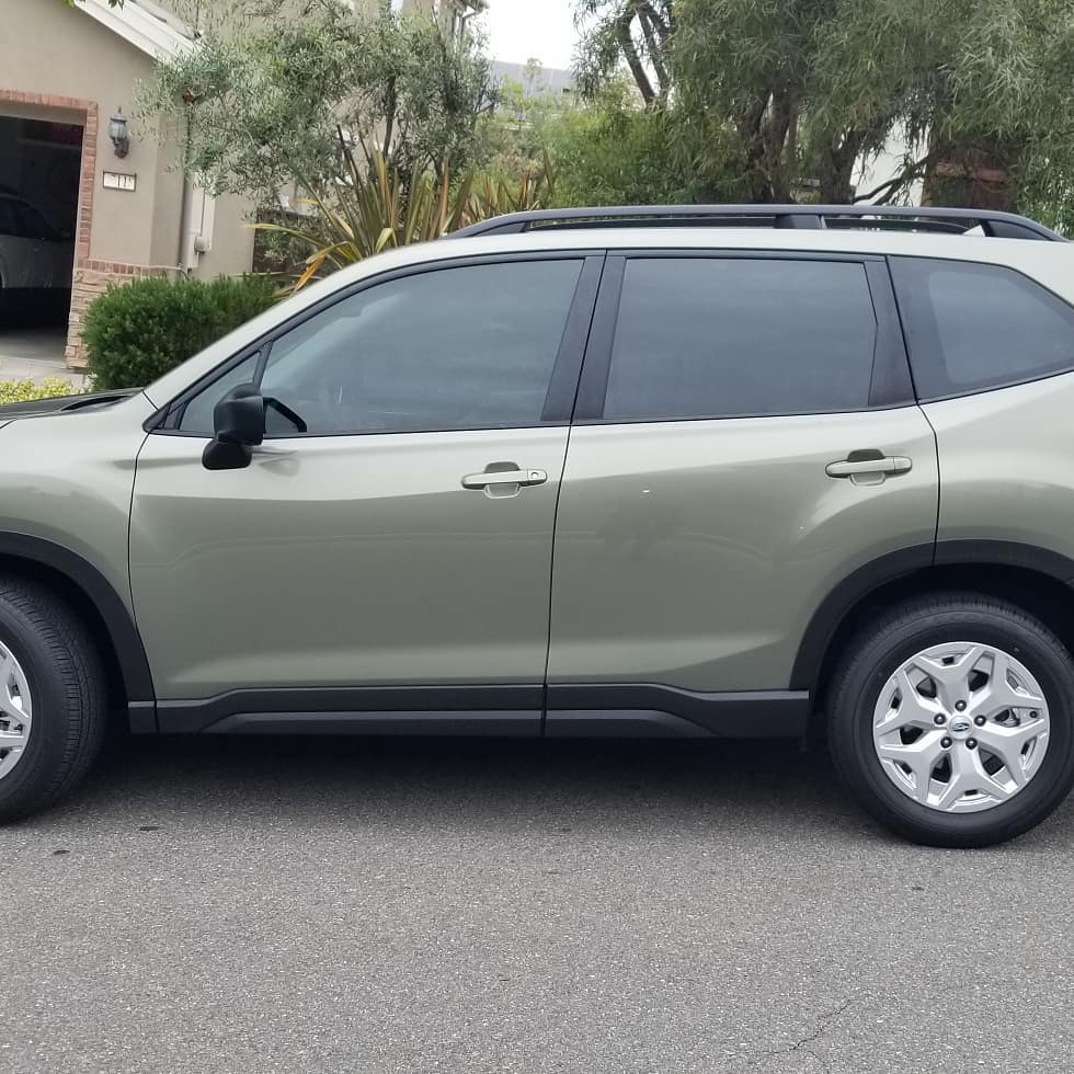 Green SUV parked on a paved road in front of a house.