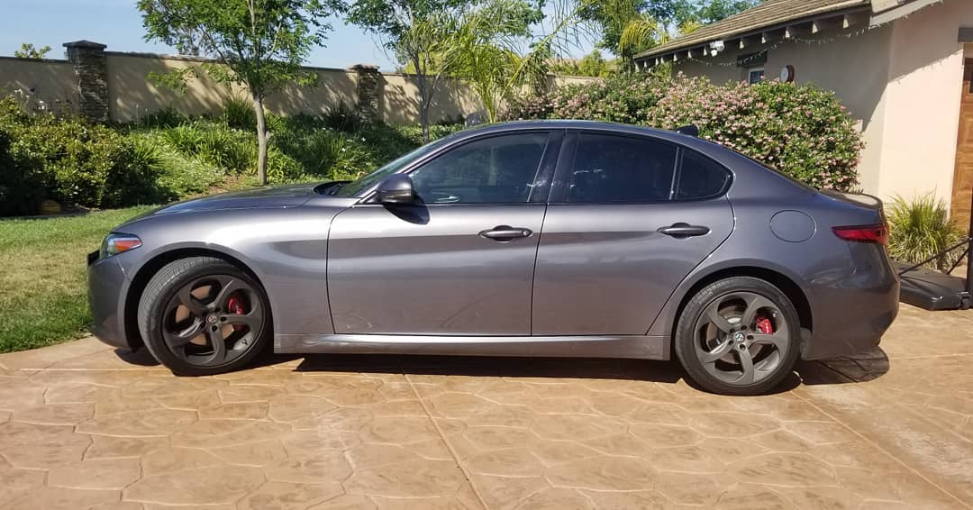 Gray Alfa Romeo Giulia parked on a concrete driveway with tinted windows and red brake calipers.