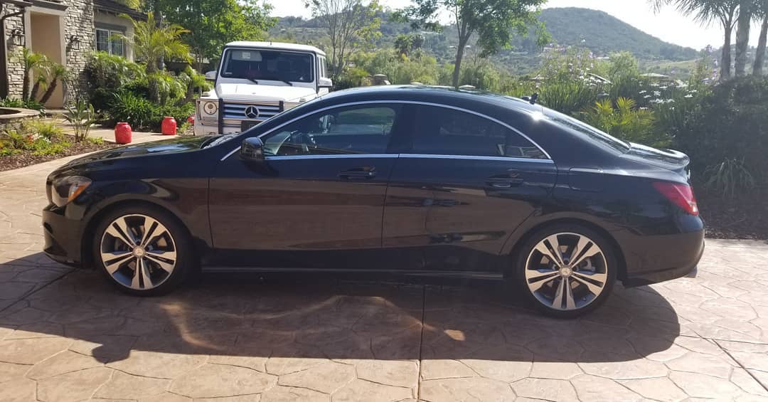 Black Mercedes coupe parked on a driveway, with a white SUV in the background. Sunny day.