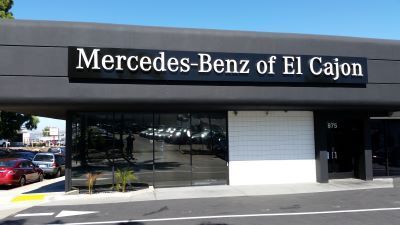 Mercedes-Benz of El Cajon storefront with large sign. Black building, glass windows, cars parked outside.