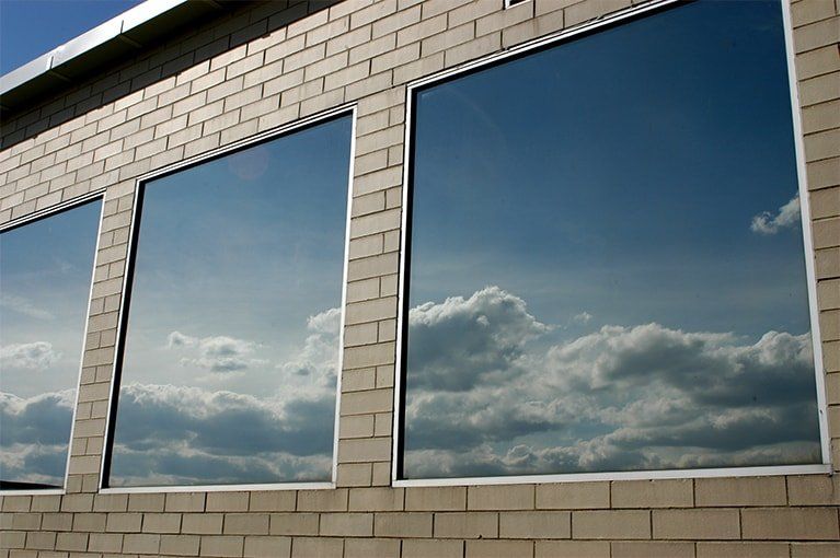 Three large windows in a brick wall reflecting a cloudy blue sky.