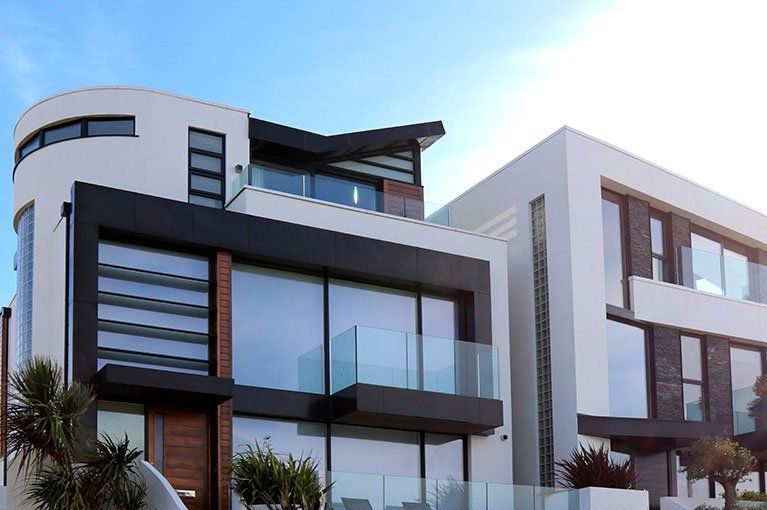 Modern white and black multi-story house with glass balconies, clear blue sky.