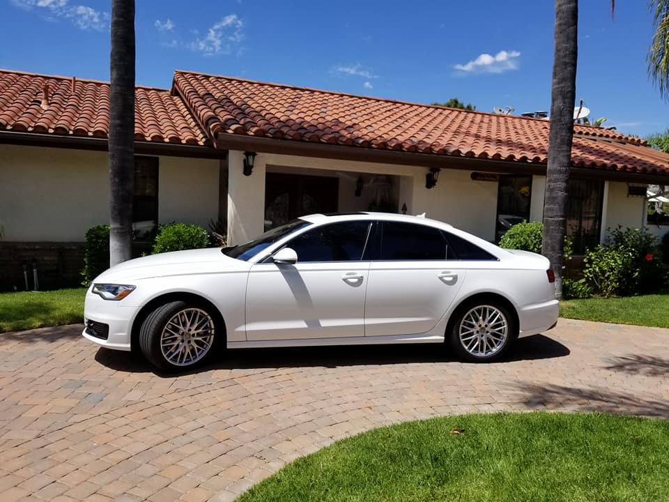 White Audi sedan parked in front of a house with a red tile roof on a sunny day.