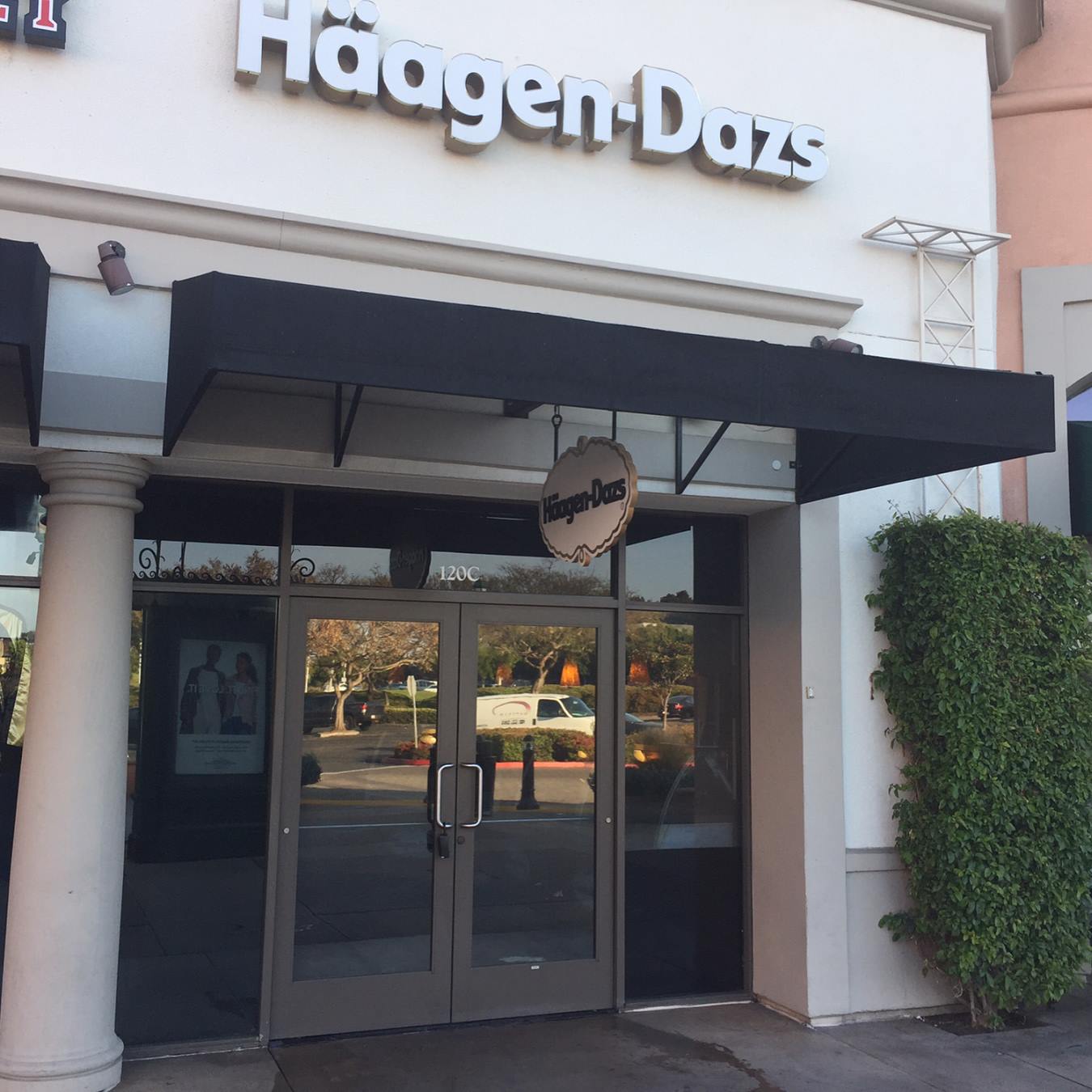 Exterior of a Häagen-Dazs store with a black awning and glass doors. A hanging sign reads Häagen-Dazs.