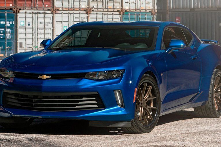 Blue Chevrolet Camaro sports car parked in front of shipping containers.