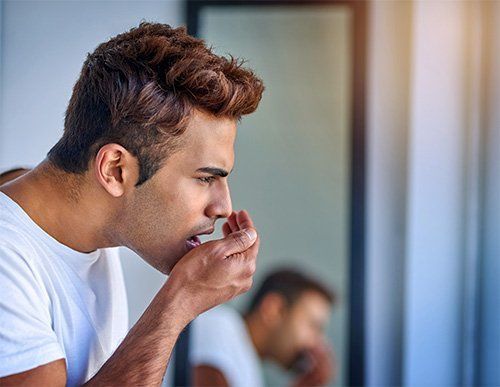 Addressing Common Dental Problems Young man checking his breath