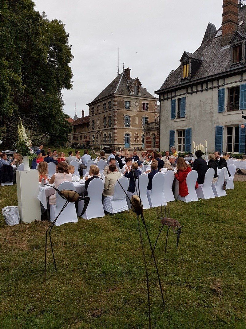 Een groep mensen zit aan tafels in het gras voor een groot gebouw