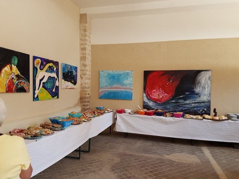 Een vrouw in een geel shirt staat voor een buffet tafel in een kamer met schilderijen aan de muur