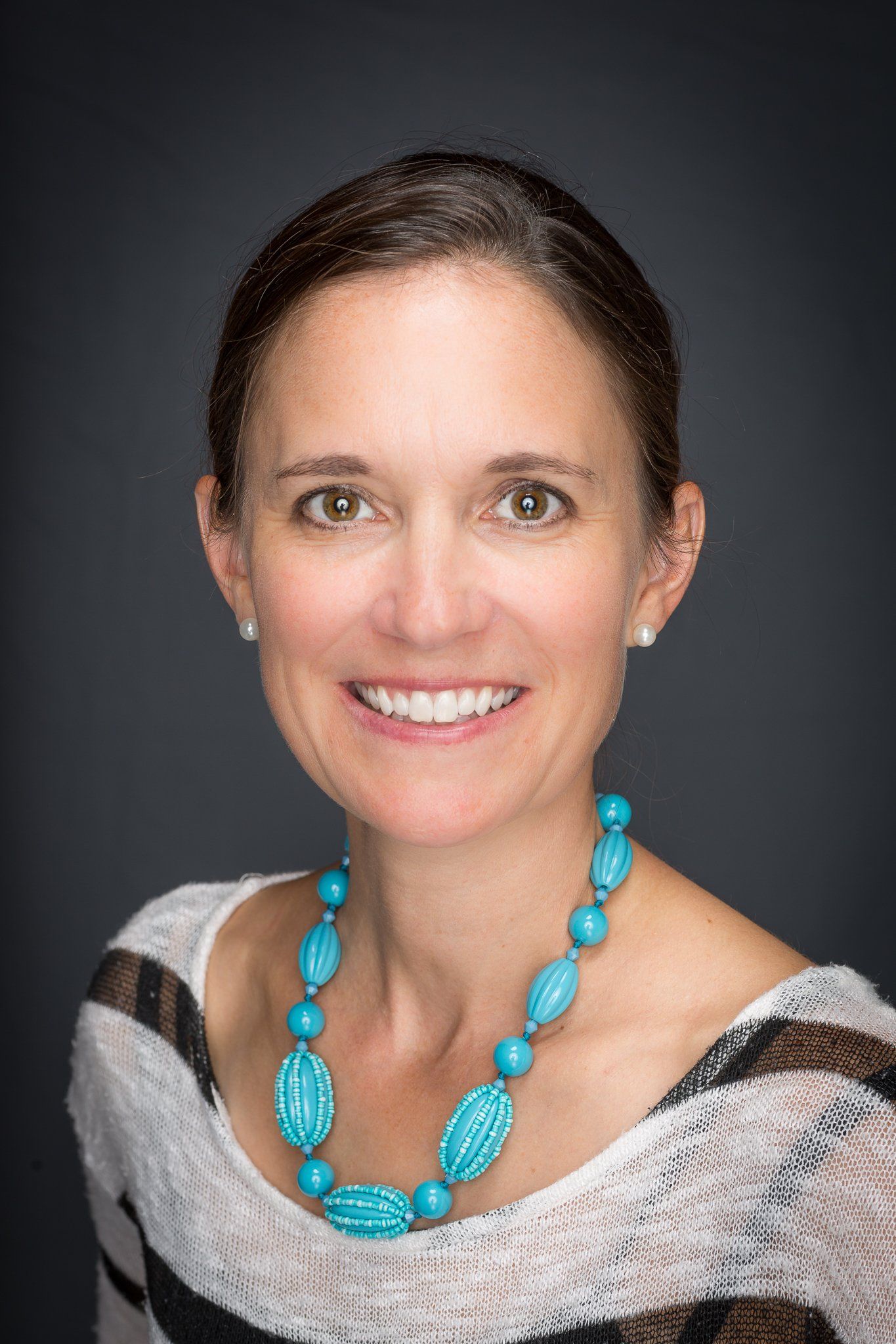 A woman wearing a turquoise necklace and earrings is smiling for the camera.