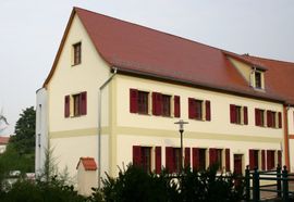 Cremefarbenes Haus mit rotem Dach und Fensterläden, vom Vorgarten aus gesehen