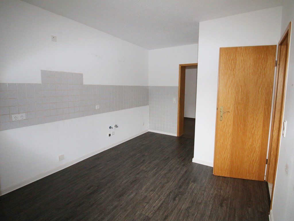 Leerer weißer Raum mit grauen Fliesen an der Küchenrückwand, dunklem Holzboden und einer offenen Holztür