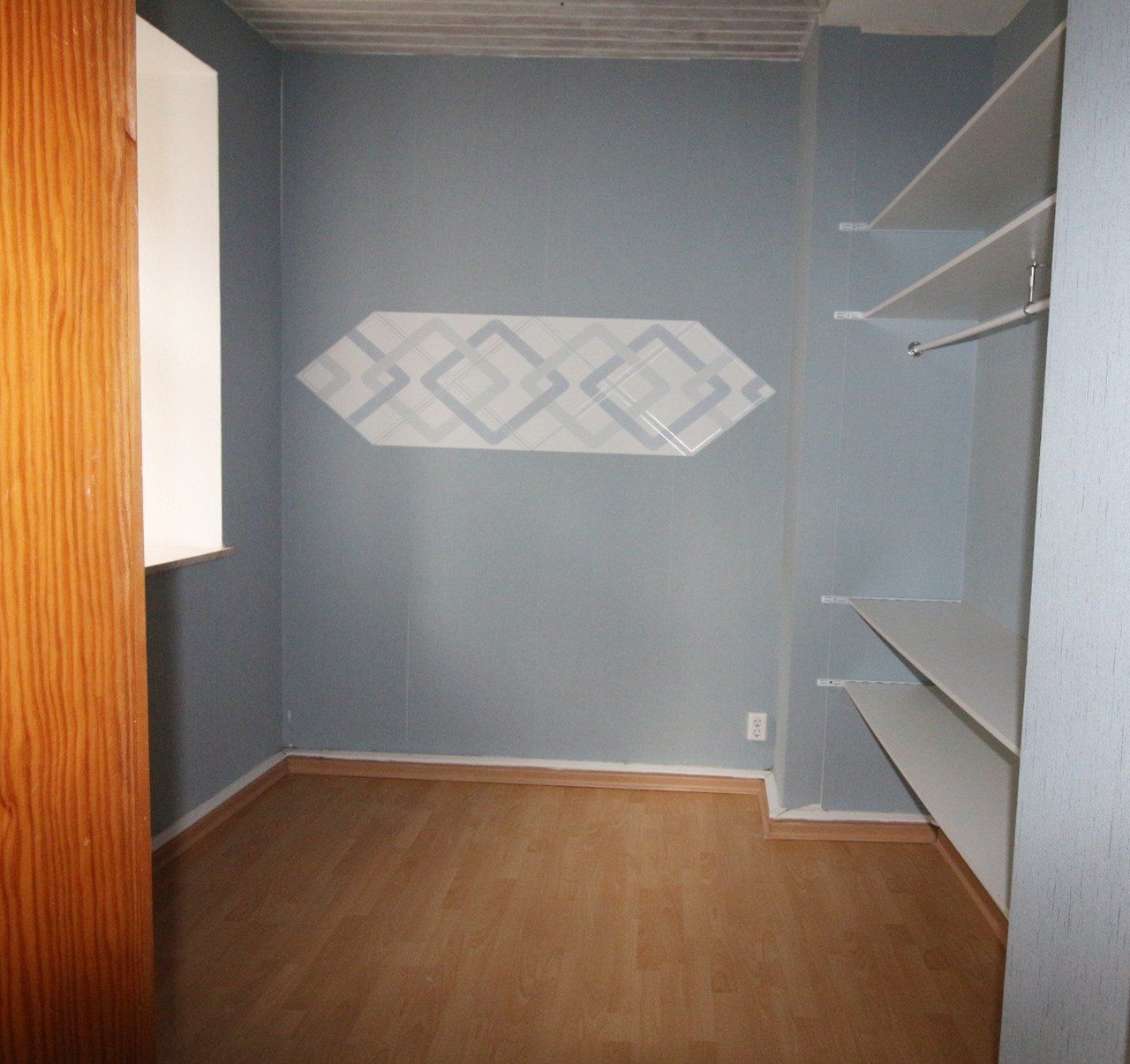 Leerer kleiner Schrank mit grauen Wänden, Holzboden und eingebauten Regalen auf der rechten Seite.