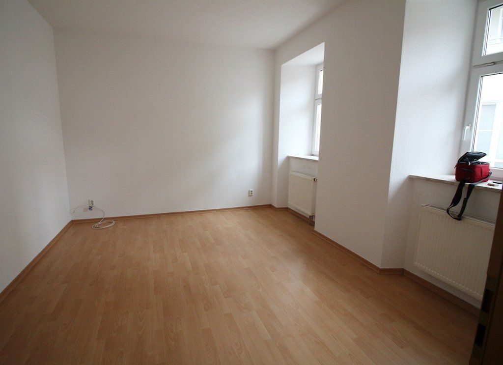 Leerer weißer Raum mit Holzboden und zwei Fenstern über den Heizkörpern.