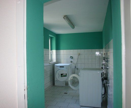 Kleiner Waschraum mit Waschmaschine, Waschbecken und Toilette in einem türkisfarbenen Innenraum