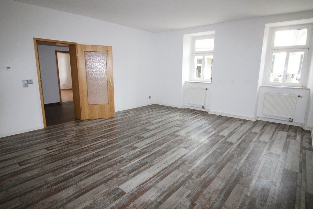 Leerer weißer Raum mit Holzbodenoptik, zwei Fenstern und einer offenen Holztür