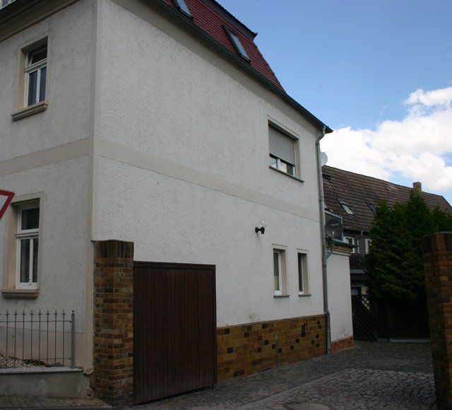 Weißes Haus mit rotem Dach, hölzernem Garagentor und gepflasterter Auffahrt in einem Wohngebiet.